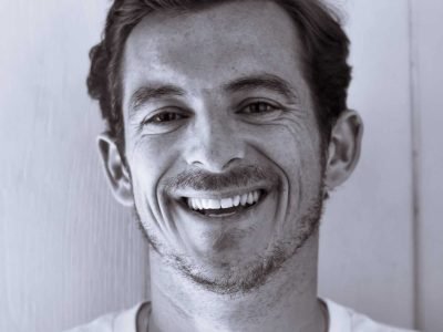 Sonriente joven con cabello peinado hacia atrás en fondo de madera.